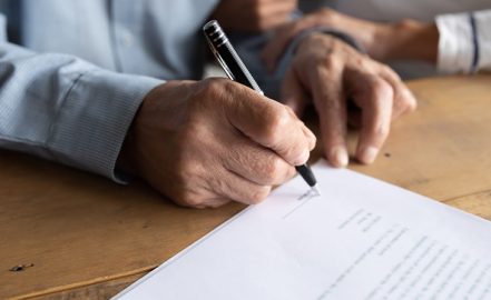 close up of older man signing estate planning papers