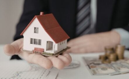 A person in a suit holding a miniature housing model