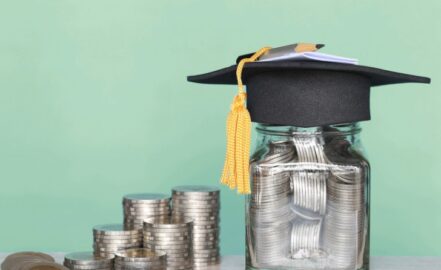 A graduation hat on a glass bottle with a stack of coins