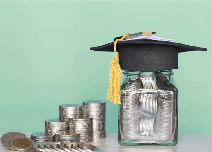 A graduation hat on a glass bottle with a stack of coins